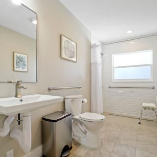A spacious and accessible bathroom with a large mirror, sink, toilet, and window.