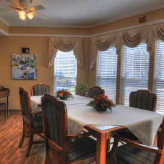 A well-lit dining room with a large table and chairs, featuring elegant decor and multiple windows.