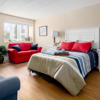 A cozy and well-lit bedroom featuring a red sofa, striped bedding, and decorative pillows.