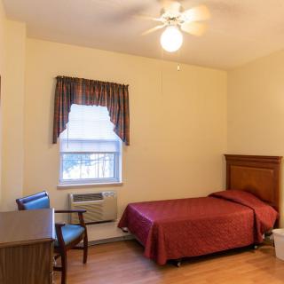 A cozy bedroom with a single bed, desk, chair, and window adorned with curtains.