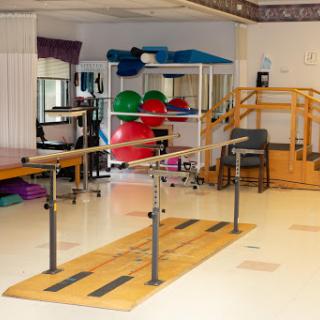 A well-equipped physical therapy room featuring parallel bars, exercise balls, and a staircase for rehabilitation activities.