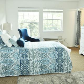 A bright bedroom with patterned bedding and a comfortable chair by the window.