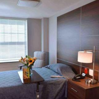 A hospital room with a bed, nightstand, and vase of flowers near the window.