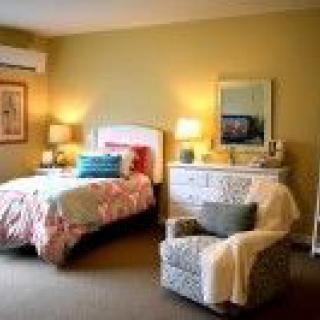 A cozy bedroom with a bed, dresser, and armchair, warmly lit by lamps.
