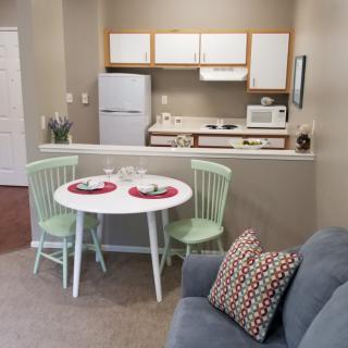 A small apartment kitchen with a dining area, featuring a table set for two, a compact refrigerator, and essential cooking appliances.