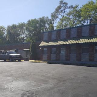A view of a motel with a parking lot, surrounded by trees on a sunny day.