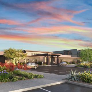 A modern building with a parking lot and vibrant landscaping under a colorful sunset sky.