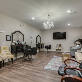 A modern salon interior featuring stylish chairs and mirrors, with a chandelier and wooden flooring.