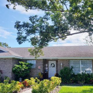 A single-story brick house with a well-maintained front yard and large tree under a clear blue sky.