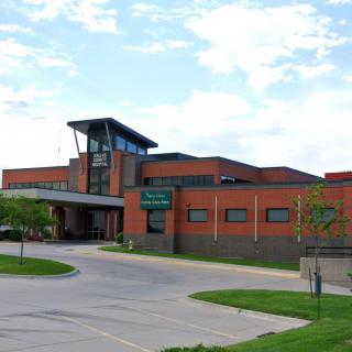 A modern brick hospital building with a prominent entrance under a partly cloudy sky.