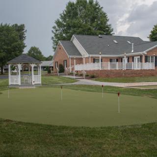 A serene backyard featuring a well-maintained putting green and a gazebo, surrounded by lush greenery.