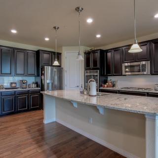 A modern kitchen with dark cabinets, hardwood flooring, and stainless steel appliances.
