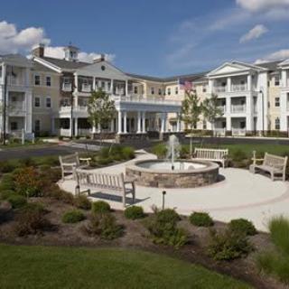A beautiful residential building with a landscaped garden and benches surrounding a fountain under a clear blue sky.