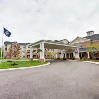 A large building with a covered entrance and a driveway, featuring landscaping and a flagpole.
