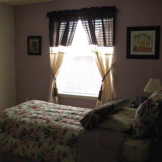 A cozy bedroom with a neatly made bed, framed art on the walls, and a window adorned with curtains.