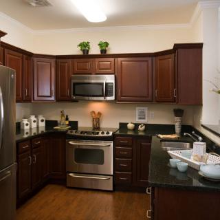 A modern kitchen with wood cabinets, stainless steel appliances, and green countertops.