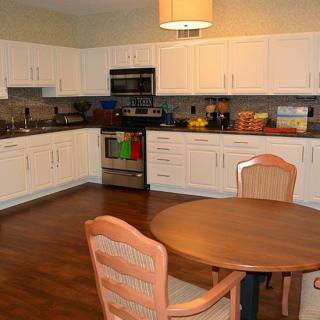 A modern kitchen and dining area with white cabinets, a round wooden table, and chairs on a wood floor.