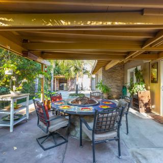 A cozy outdoor patio area with a table and chairs set under a covered pergola, surrounded by lush greenery.