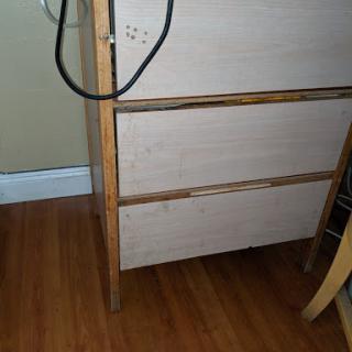 A wooden dresser with a minimal design, showcasing its drawers and standing on a hardwood floor.