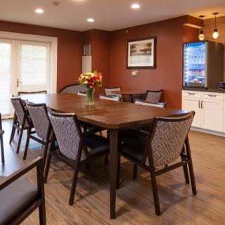 A cozy dining room with a large wooden table and chairs, decorated with flowers.