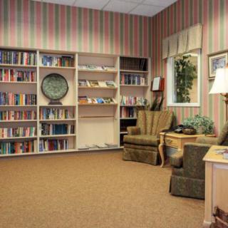 A cozy reading room with bookshelves, armchairs, and a lamp.