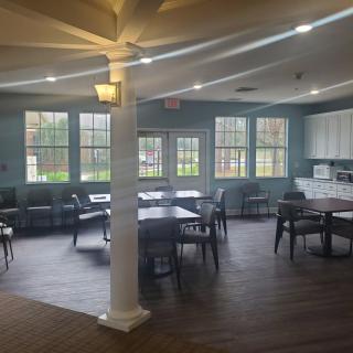 A spacious and well-lit dining area with tables and chairs, adjacent to a kitchenette.