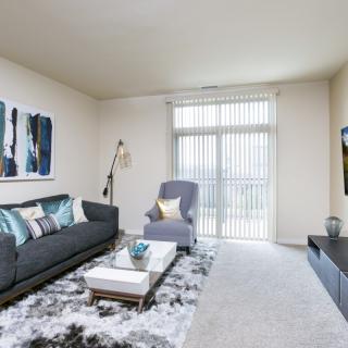 A modern living room with stylish decor, featuring a sofa and armchair, large artwork on the wall, and a floor lamp next to a window with vertical blinds.