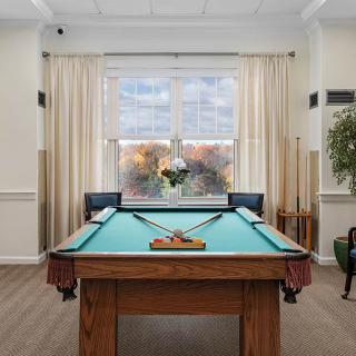 A cozy game room featuring a billiards table with cues and balls, set near a window with light curtains.
