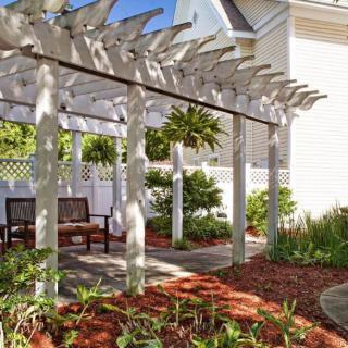 A charming garden pergola with benches, surrounded by lush greenery and landscaping.