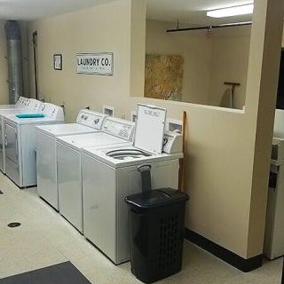 A spacious laundry room with multiple washing machines and a trash can.
