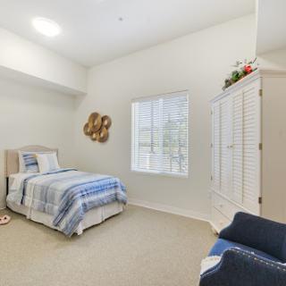 A cozy and well-lit bedroom featuring a single bed with blue and white bedding, complemented by a decorative wardrobe and natural light from the window.