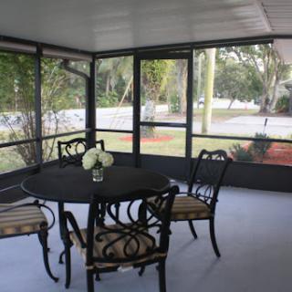 A cozy screened porch featuring a round table with elegant chairs and decorative flowers, perfect for enjoying natural light.