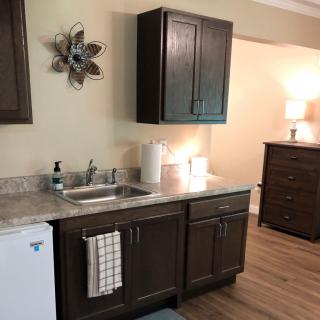 A small kitchenette with a sink, cabinets, and countertop in a cozy room setting.