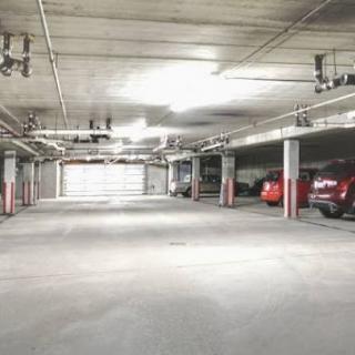 An empty parking garage with a few cars under bright overhead lights.