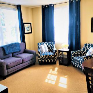 A cozy living room with a sofa, patterned armchairs, and blue curtains.