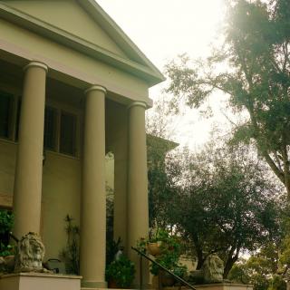 A classical building with tall columns surrounded by trees in sunlight.