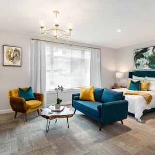 A modern living and bedroom space featuring elegant furnishings with a stylish blue sofa, mustard armchair, and chic chandelier.