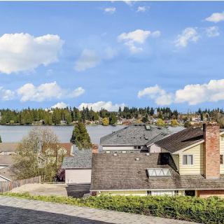 A scenic view of suburban rooftops with a backdrop of a lake and trees under a partly cloudy sky.