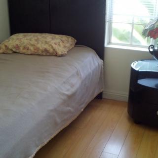 A minimalist bedroom with a single bed, pillow, nightstand, and window.