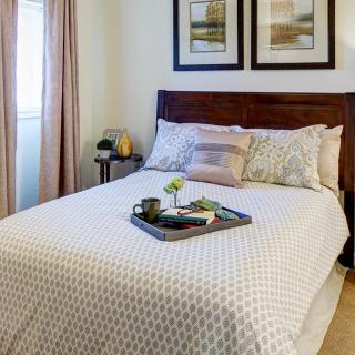 A cozy bedroom setup with a neatly made bed and decorative pillows, featuring a stylish wooden headboard and framed art on the wall.