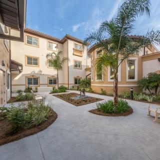 A modern courtyard with pathways, landscaping, and palm trees surrounded by a multi-story building.