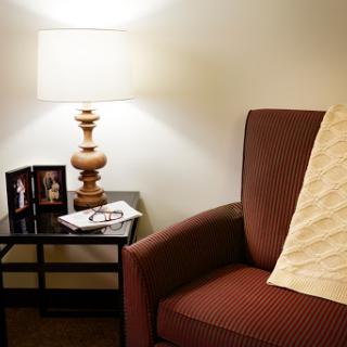 A cozy corner of a living room featuring a comfortable chair, a side table with a lamp, and framed photographs.