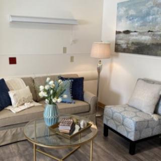A cozy living room with a sofa, armchair, and a glass coffee table adorned with a vase of flowers.