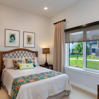 A cozy bedroom with a stylish bed, decorative pillows, side lamp, and large window overlooking a garden.