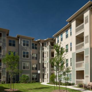 A modern apartment building with balconies and a landscaped courtyard on a sunny day.