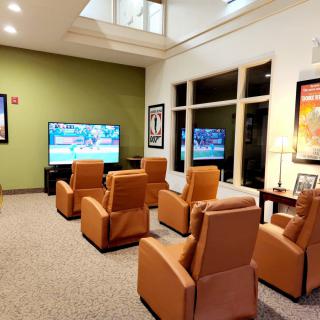 A cozy lounge with comfortable chairs facing a large television, perfect for relaxing or waiting.