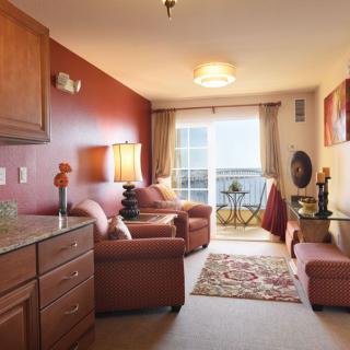 A cozy and warmly decorated living room featuring comfortable armchairs, a sofa, a coffee table, and decorative items, with natural light streaming in through the window.