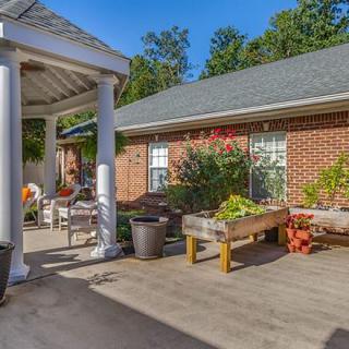 A sunny patio with potted plants and outdoor furniture next to a brick building.