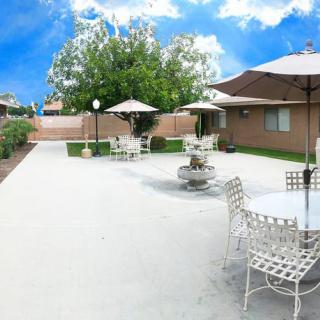 A spacious backyard patio with tables, chairs, and umbrellas under a bright blue sky.