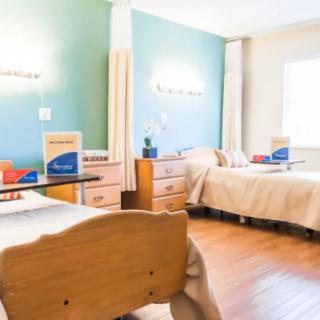 A well-lit hospital room with two beds and wooden furniture.